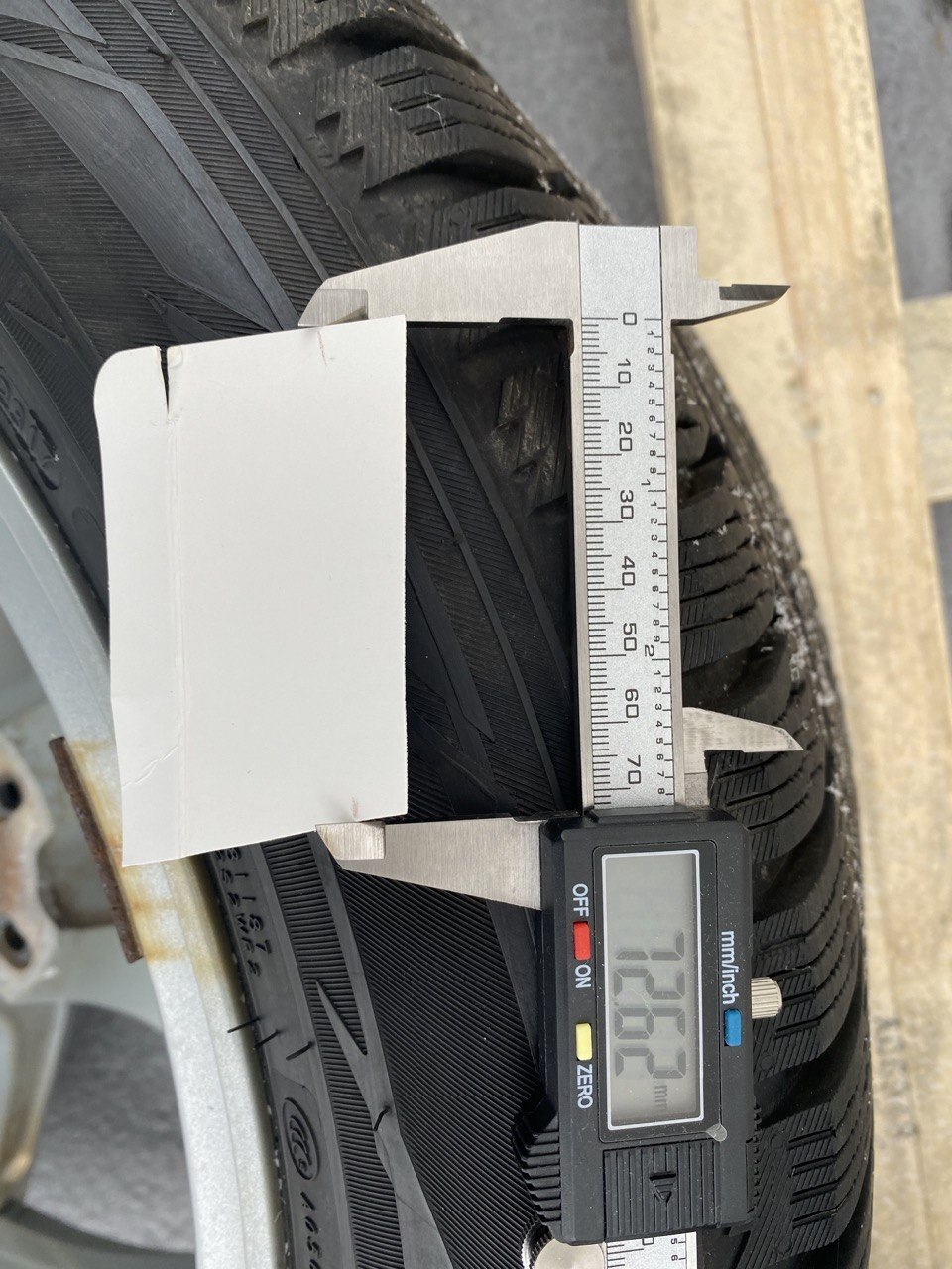 Measuring wheel center bore with cardboard wedge and calipers